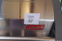 Close-up of stainless steel lid with red Coleman logo and auction tag number 57.