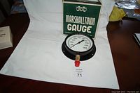 Photo of the Marshalltown pressure gauge placed on a white background showing the face of the gauge and its box behind it.