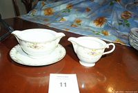 Gravy boat and creamer shown from side angle on table, floral tablecloth in background