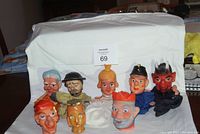 Full view of 9 assorted old hand puppets including an elderly man, policeman, devil, clown, and other characters arranged on a white cloth.