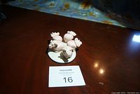 Four pink ceramic pig figurines on a white oval base, photographed from above showing their arrangement.