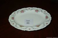 Oval white china platter with pink rose floral pattern and silver rim accents photographed on wood surface with auction lot tag.