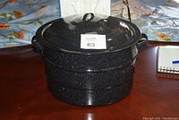 Side view of black speckleware canning pot with lid on wooden table