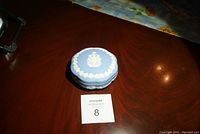 Top view of the oval blue Wedgewood covered dish with white relief design on lid, placed on wooden surface with lot number card
