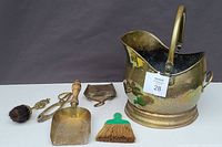 Full view of the brass coal scuttle coal bucket alongside the miscellaneous fireplace tools including brass dustpan, small broom, brush with wooden handle, brass tongs, and small shovel.