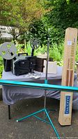 Wide shot showing all items on table including projector with reels, carousels, screen tripod, and original screen box.