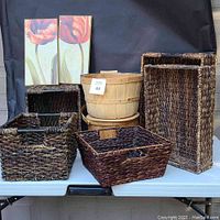 Photo showing seven baskets arranged on table with two vertical tulip wall art prints behind.