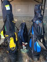 Photo of two junior golf bags, one black and yellow 'Stix' bag and another black and blue 'Confidence' bag with a male golfer door stop between them