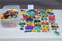 Wide view of approximately 50 diecast toy cars arranged on a table, showing variety of colors and styles including classic, race, and utility vehicles.
