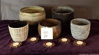 Front view of five pots and five red jeweled votive holders on dark fabric surface