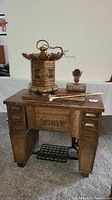 Full front view of cabinet showing drawers, treadle pedal, brass lantern, and accessories on top.