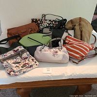 Lot of nine purses arranged on white cloth on table, showing variety in style, color, and size including floral, striped, and solid prints.