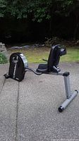 Full side view of the SportsArt recumbent bike on outdoor pavement showing seat, pedals, and frame.