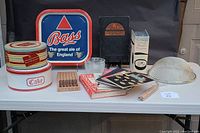 Photo showing the entire collection of vintage kitchen items on a white table, including tins, tray, cookbooks, metal strainer, wooden steak cutters, and lemon squeezers.