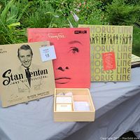 Photo showing three vintage record album covers including Stan Kenton and His Orchestra, a red cover with a woman's face, and a yellow Broadway-related album.
