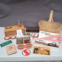 Wide shot of entire lot showing all items including boxes, tins, basket, pinking shears box, various needle packs, tin containers, and sewing accessories.