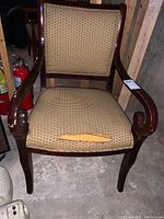 Front view of wooden arm chair with visible wear and tear on seat upholstery.