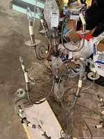 Photo showing the full chandelier with steel curved arms, candle-style holders, and the base glass decorative piece in a garage setting with various items in the background.