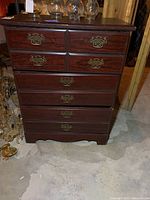 Front view of four drawer wooden chest with brass-colored handles and visible surface scratches.