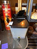 Tall Luzianna Iced Tea metal dispenser and a square plastic drink dispenser with black lid and spigot.