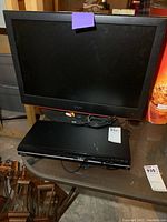 Photo shows 25 inch Viore flat-screen TV on top with cord plugged in, placed on wooden shelf with a Toshiba DVD player underneath without remote.