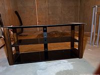 Front view of the media table showing three smoky glass shelves supported by wood side panels and central black metal support with cord minder holes.