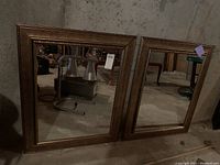 Two matching rectangular mirrors with gold decorative edges positioned side by side against a concrete wall.