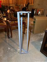 Photo showing front and side view of the metal butcher paper holder frame standing on concrete floor, white paint with minor wear.