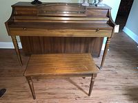 Front view of the Whitney upright piano with matching bench on wood floor.