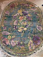 Full view of the oval floral rug showing the overall design and condition on concrete floor.