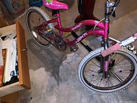 Pink girls bike with floral decals and white tires on a concrete basement floor
