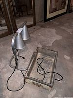 Stainless steel industrial steamer with attached heat lamp and power cords visible on a floor surface