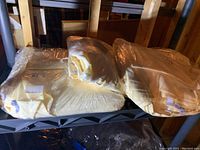 Multiple yellow tablecloths folded and wrapped in clear plastic, placed on a shelf in a basement.