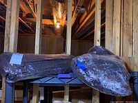 Four packages of tightly wrapped dark brown cloth table napkins on a basement shelf.