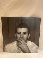 Front cover of Arctic Monkeys vinyl record showing a black and white close-up portrait of a man smoking a cigarette.
