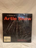 Front cover of the vinyl record album displaying the title "A Tribute to Artie Shaw" with an image of a clarinet and the Eros label logo.