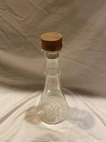 Clear glass decanter with teak wood stopper on neutral background showing shape and wood finish of stopper.
