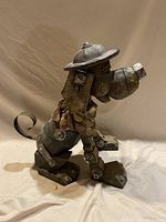 Side view of dog sculpture showcasing mechanical leg details, curled tail, and hat.