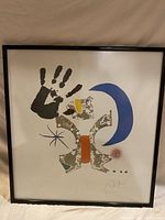 Full view of Joan Miro lithograph poster in black frame, showing abstract colorful shapes and black handprint on white background.