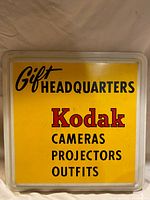 Front view of the Kodak advertising sign showing yellow background with black and red text that reads 'Gift Headquarters Kodak Cameras Projectors Outfits'