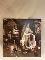 Front cover art of the Led Zeppelin 'In Through the Out Door' album showing a man lighting a cigarette in a bar scene with a woman by a jukebox in the background.