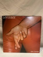 Front cover of Loverboy 'Get Lucky' vinyl record showing the album artwork of a hand with crossed fingers in red leather pants.