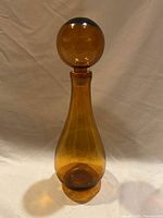 Full view of the amber glass decanter showing the teardrop shape and spherical stopper