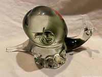 Side angle showing the snail figurine with smoky gray shell and clear glass body on a white background.