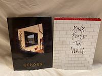 Photo showing the covers of both music books side by side on a white fabric surface, Echoes book on left and The Wall on right.
