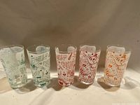 Photo showing all five glasses lined up, each with colorful retro graphics and text. No chips or cracks visible.