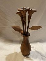 Frontal view of the teak flower vase showing three carved flowers with leaves in the vase.