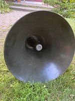 Close-up front view of the flared horn speaker painted olive drab green on grass surface.