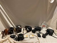 Wide shot showing all cameras, cases, film rolls, flash unit, light meter, and accessories arranged on a beige fabric background.