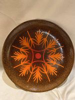 Top view showing the orange stylized leaf pattern on brown background of the circular art plate.